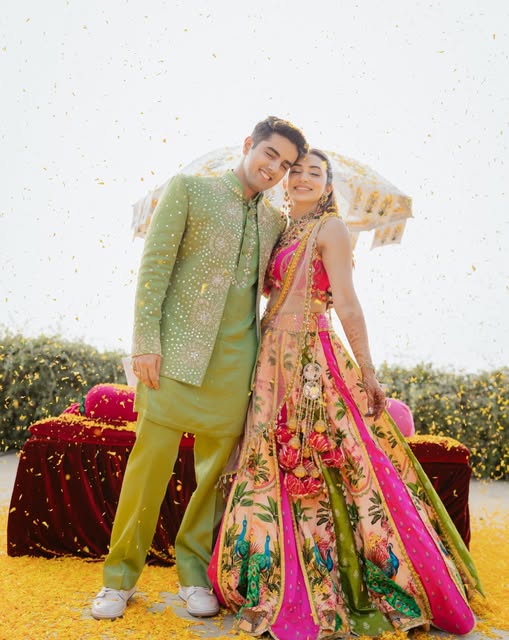 A couple in colorful outfits smiling together amid scattered marigold petals