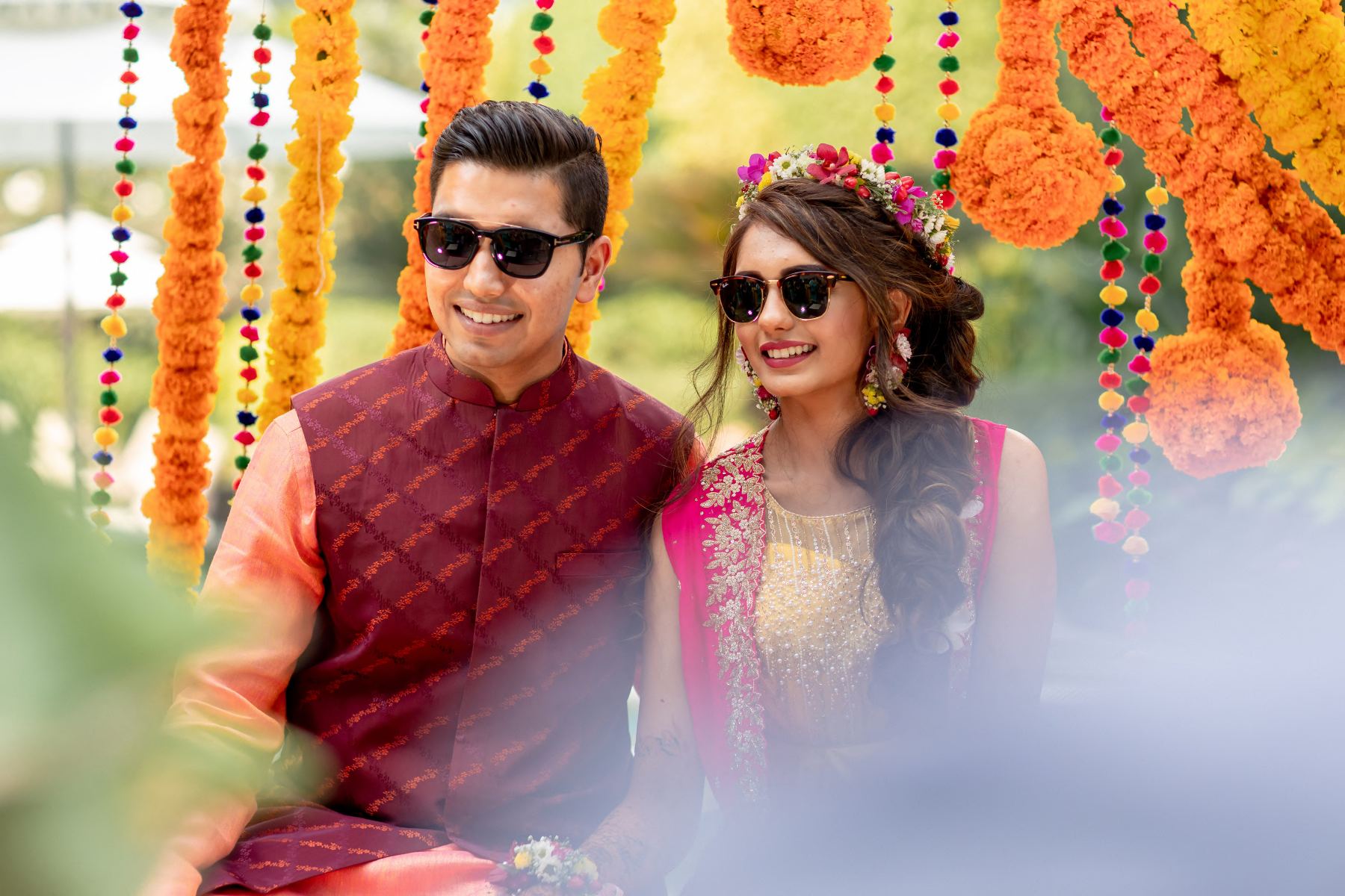 Nidhi and Rachit smiling at each other beneath hanging marigold garlands